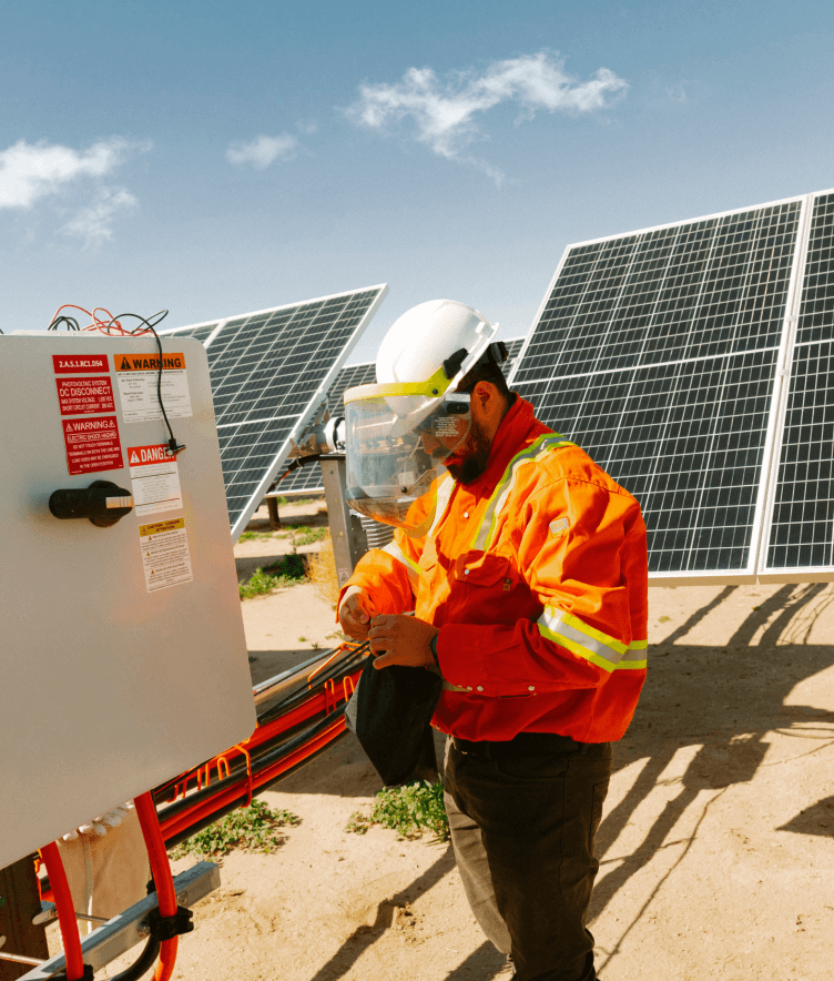 A person wearing safety equipment stands in front of solar panels. 