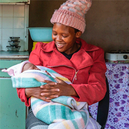 A person holding a baby, sitting on a chair in a kitchen.