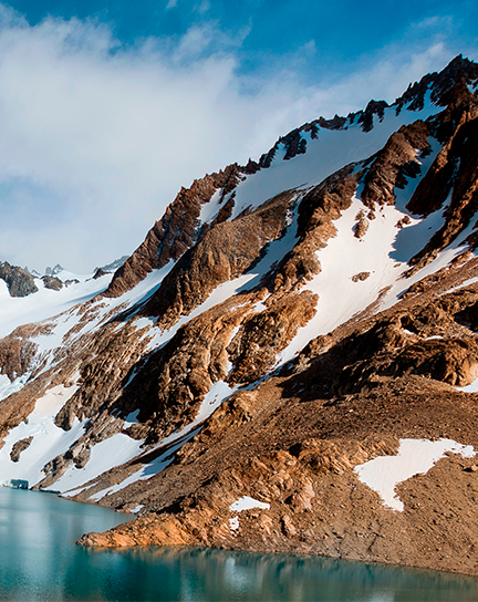 An alpine ecosystem with patchy snow on mountains and a bright, clear alpine lake.