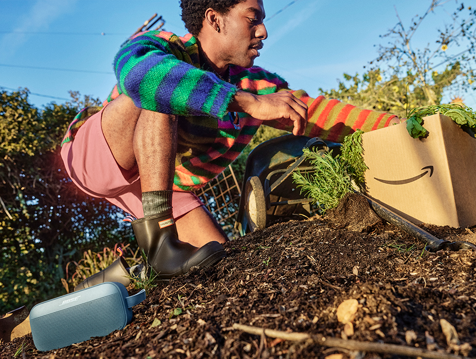 A person in a garden sorts through an Amazon box filled with produce.