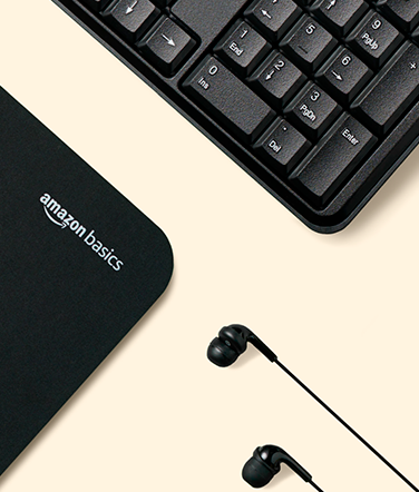 A computer keyboard, headphones, and an Amazon basics computer pad sit on a table.